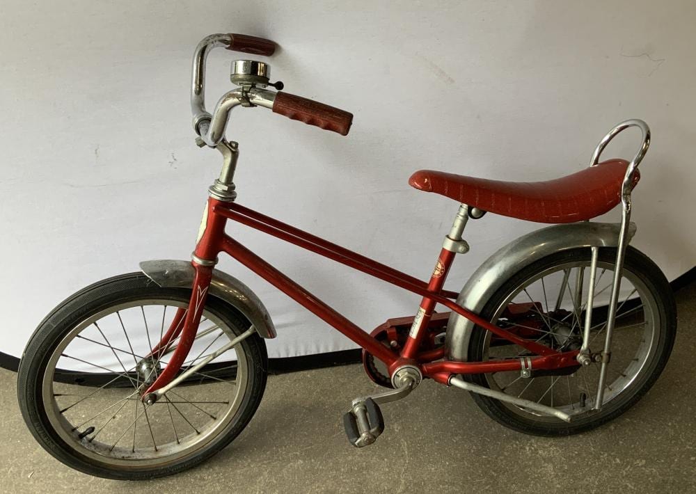 Vintage red and silver kid’s bicycle with front basket, curved handlebars, and kickstand.