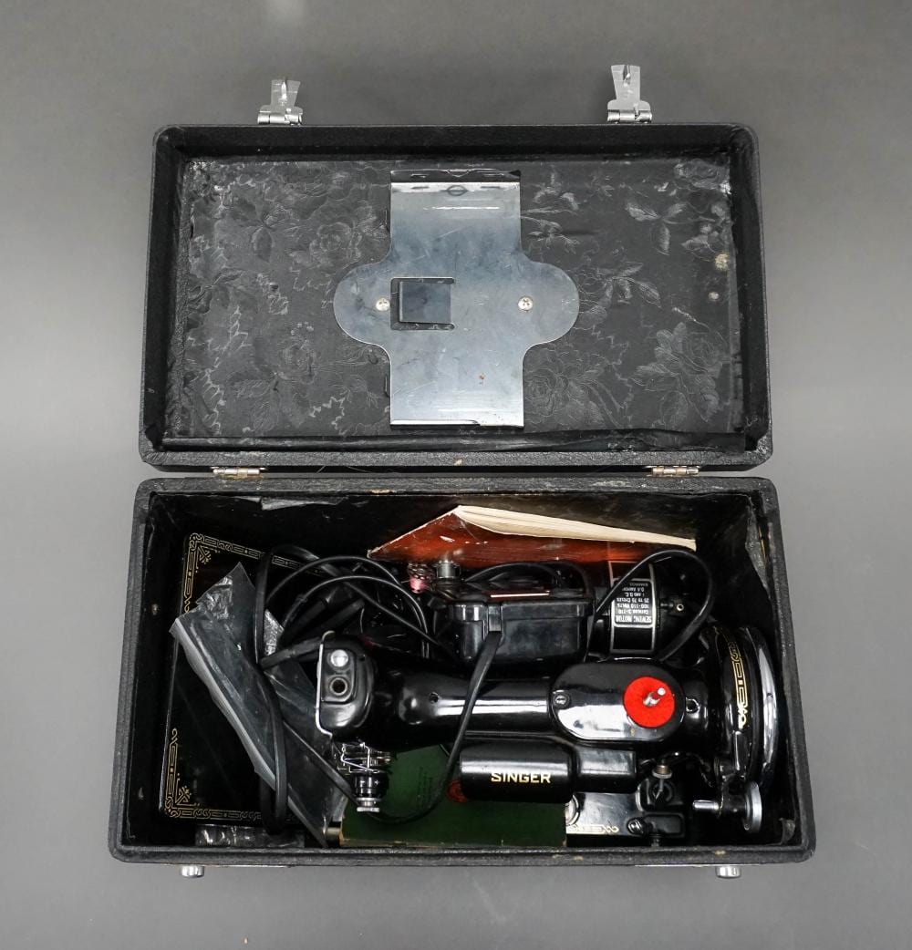Singer Featherweight sewing machine shown inside an open black carrying case with quilted top lining and fabric tools/components visible.