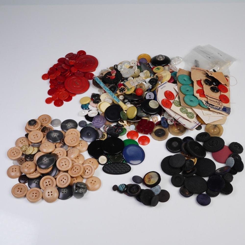 Mixed assortment of vintage-style clothing buttons in red, black, tan, and green, arranged in a group on a white background.