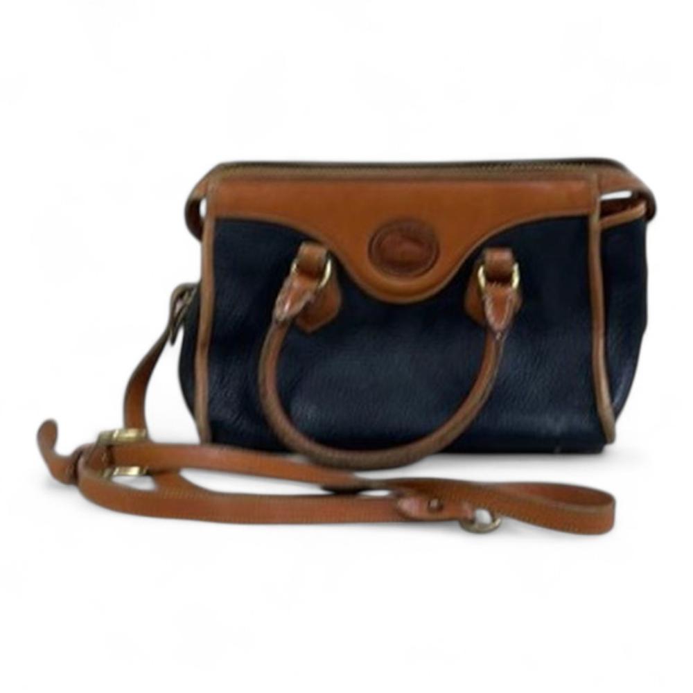 Brown and navy blue leather-style satchel with a top flap, round emblem patch, and adjustable crossbody strap