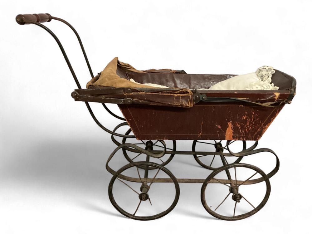 Antique-style wooden doll buggy with black metal wheels and curved handle, showing cloth and paper in the seat
