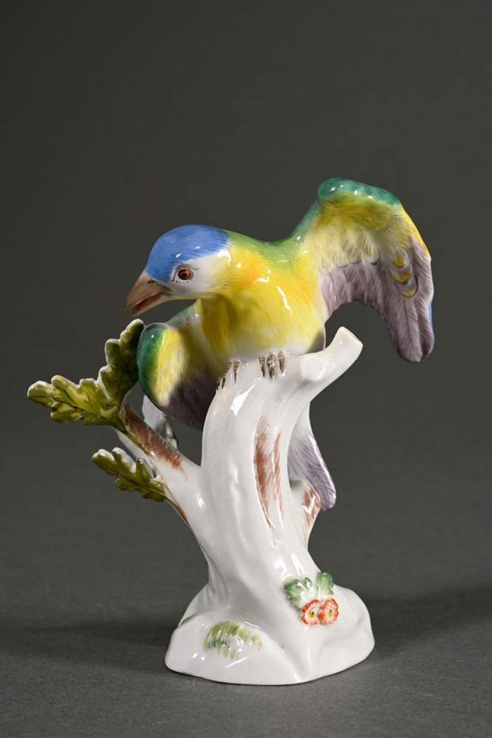 Porcelain figurine of a colorful bird standing on a white branch base with green leaves and polychrome details.
