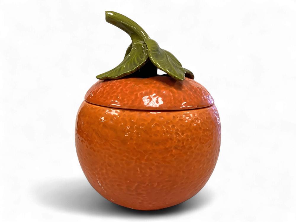 Orange ceramic cookie jar with a glossy orange textured body and a green leaf-shaped lid on a white background.