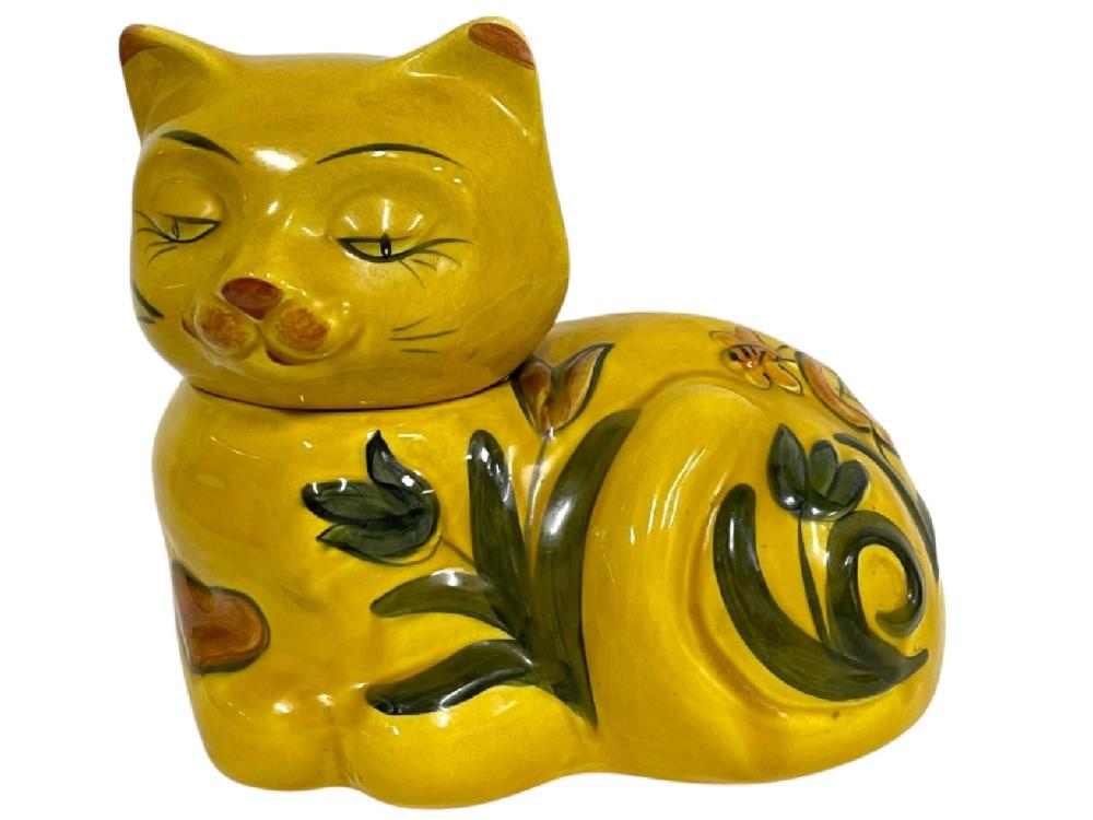 Yellow ceramic cat cookie jar shaped like a sleepy cat with closed eyes, paw held near its face, and green leaf decorations.