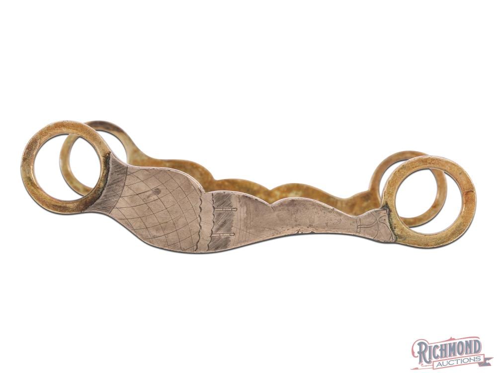Metal horse bit with two circular rings on either side and a textured center with engraved lines.
