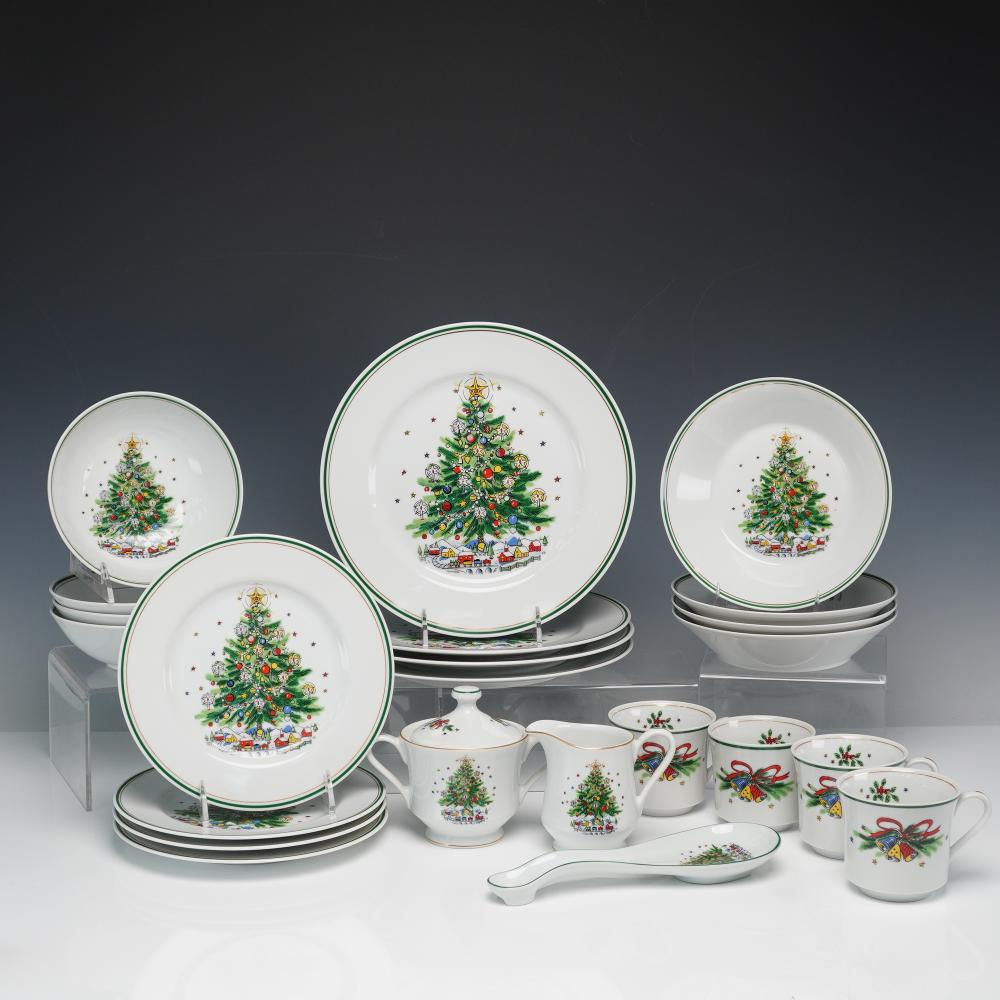 Porcelain Christmas Eve tableware set with plates, teapot, creamer and sugar bowl, and mugs decorated with a decorated evergreen tree, holly accents, and gift-m