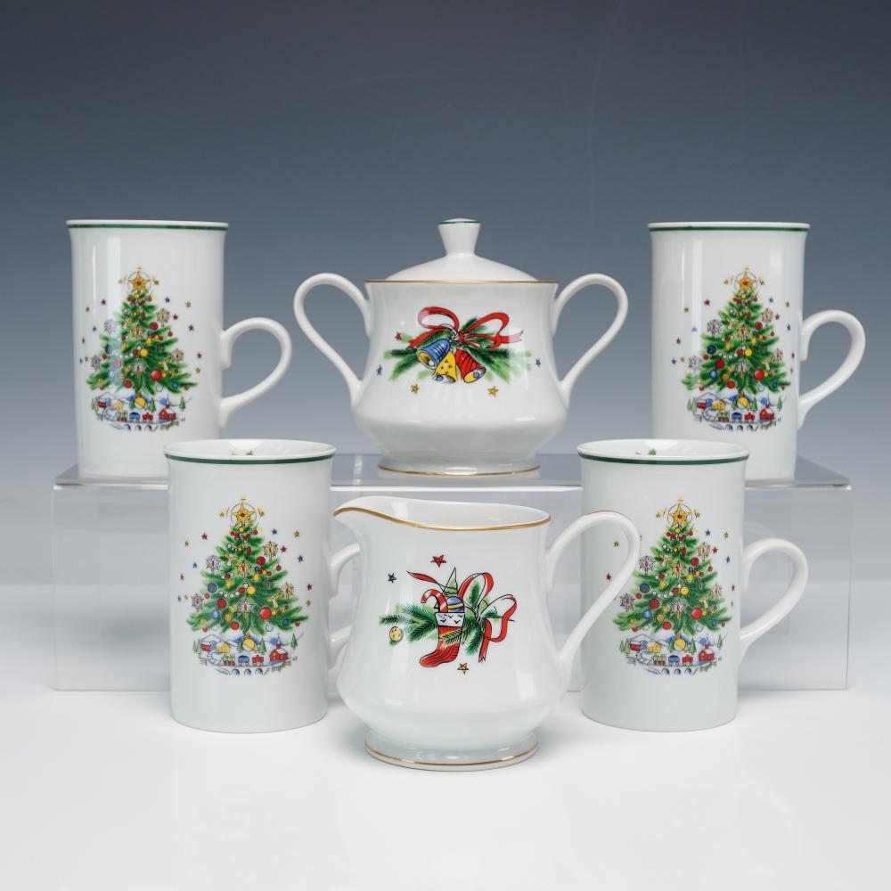 Set of five white porcelain Christmas-themed pieces with green trim and holiday tree and bell/bow designs, including a covered sugar bowl, creamer, and mugs.