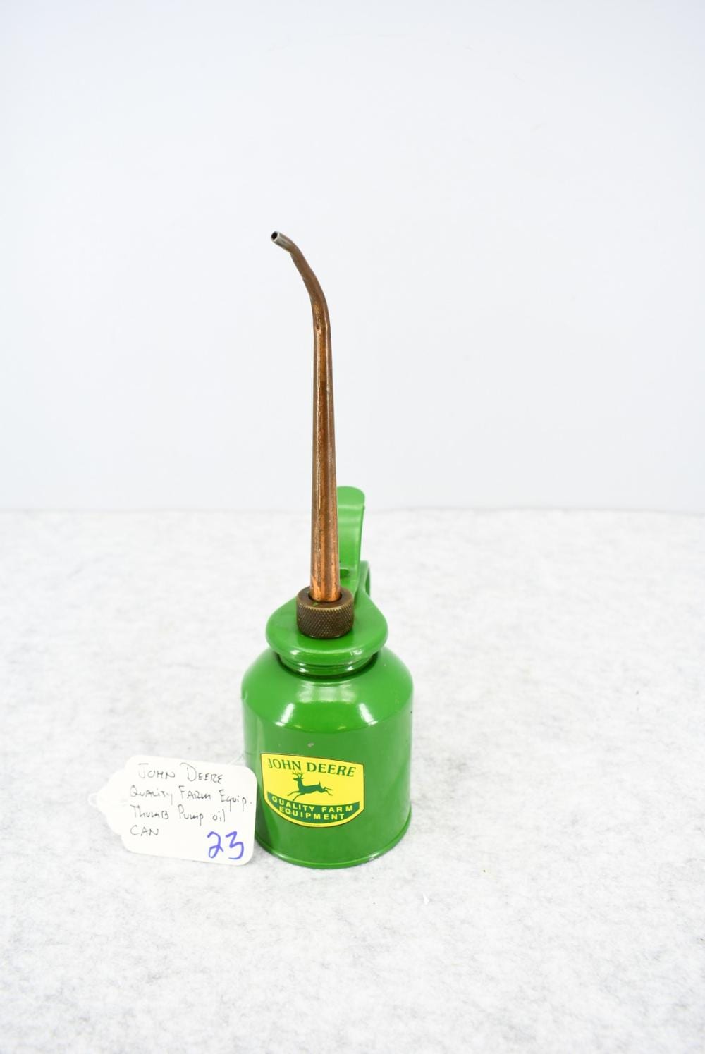 Green metal oil can with a long pump tube on top and a brass-colored nozzle collar; label reads John Deere Quality Farm Equipment.