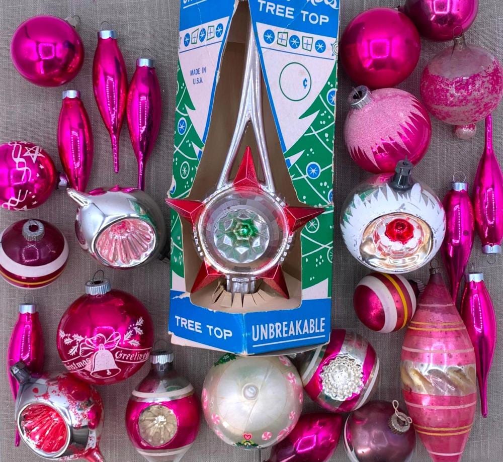 Assorted hot pink, magenta, and silver Christmas tree ornaments and a tree-topper star on a fabric background.