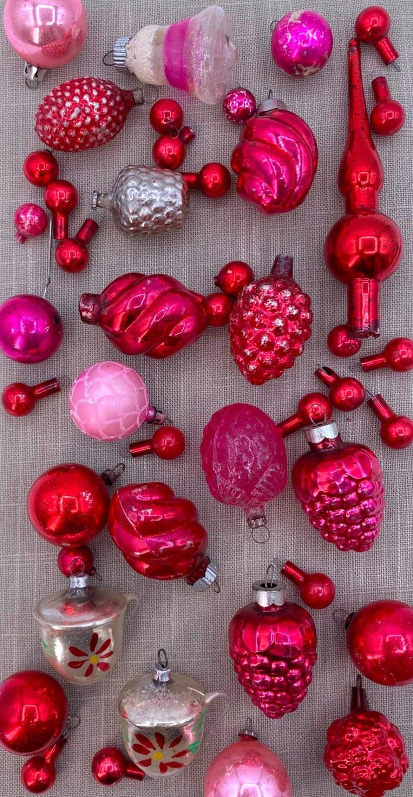 Assorted pink and red glass Christmas tree ornaments and tree-topper pieces arranged on a fabric background.