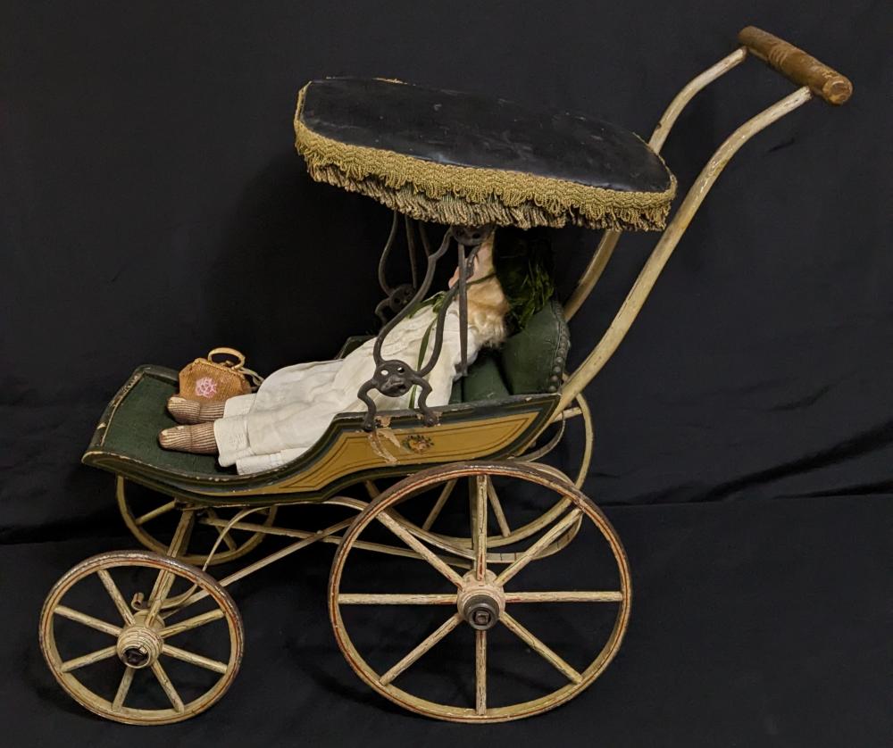 Victorian-style doll carriage buggy with dark canopy, green body, ornate gold trim, and four wire-spoke wheels.