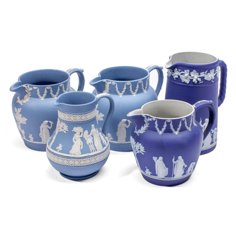 Blue ceramic creamers and pitchers with white relief-style classical figures and decorative borders, shown on a white background.