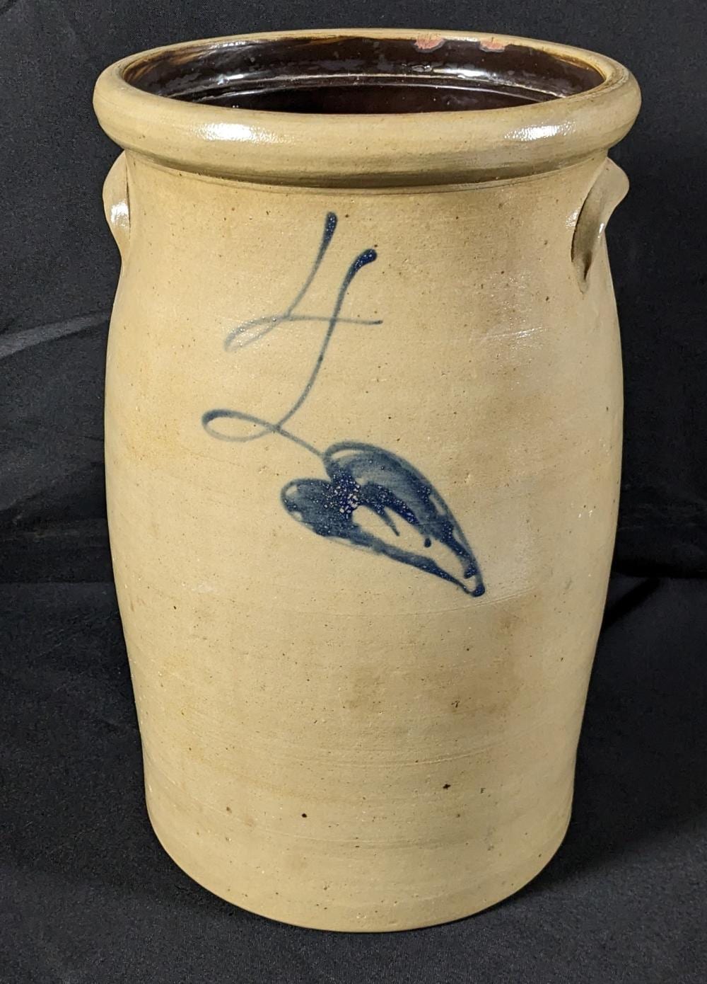 Stoneware churn crock with a round rim and side handles, cream glaze with blue leaf and stem decoration and dark interior.