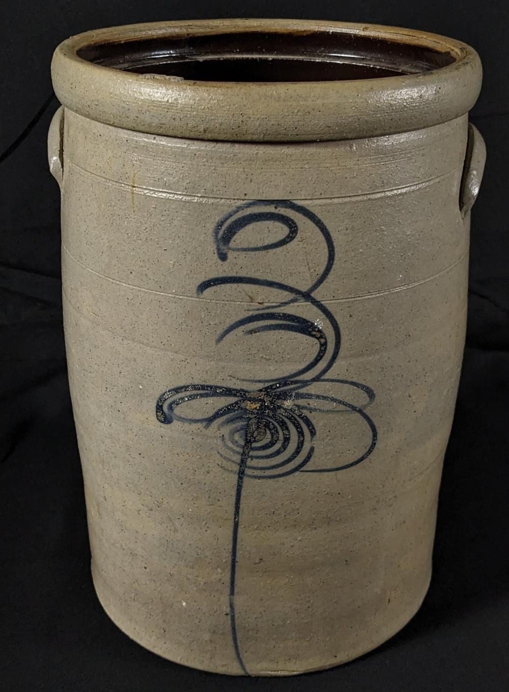 Stoneware butter churn crock with salt-glaze finish and cobalt-blue decorative motif, photographed against a dark background.