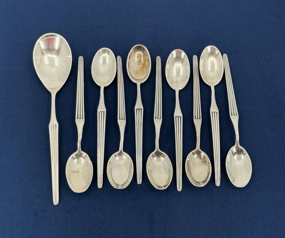 Photograph of a set of shiny silver-colored spoons and teaspoons laid out on a blue background, showing oval bowls and long handles.
