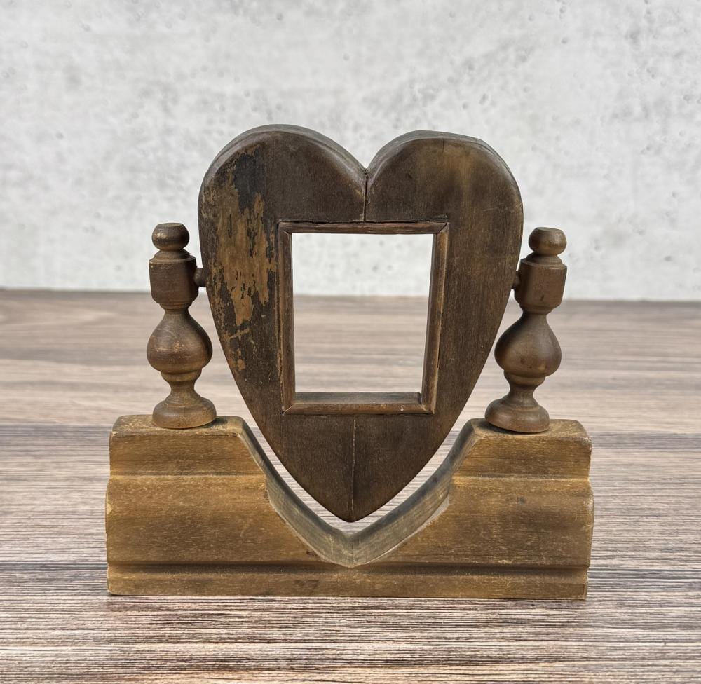 Carved heart-shaped wooden picture frame on a base with two turned candlestick-style posts on each side.