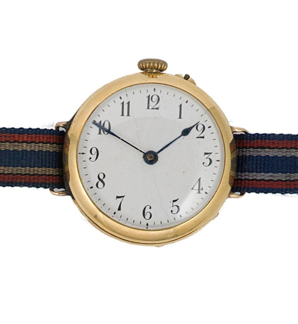 Gold-tone wristwatch with a white dial and black Arabic numerals, showing hands set near 11 and 2, on a striped fabric strap.