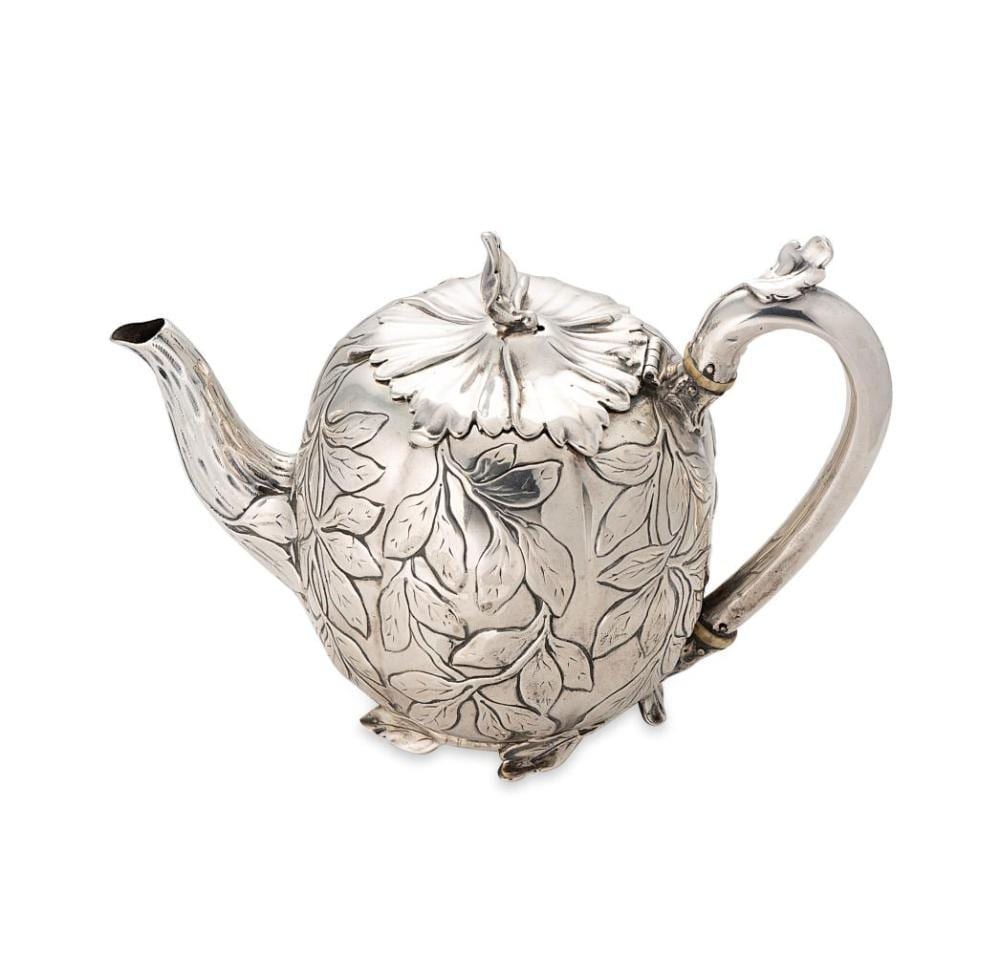 Silver teapot with a leaf and floral relief pattern, curved spout, hinged lid, and loop handle.