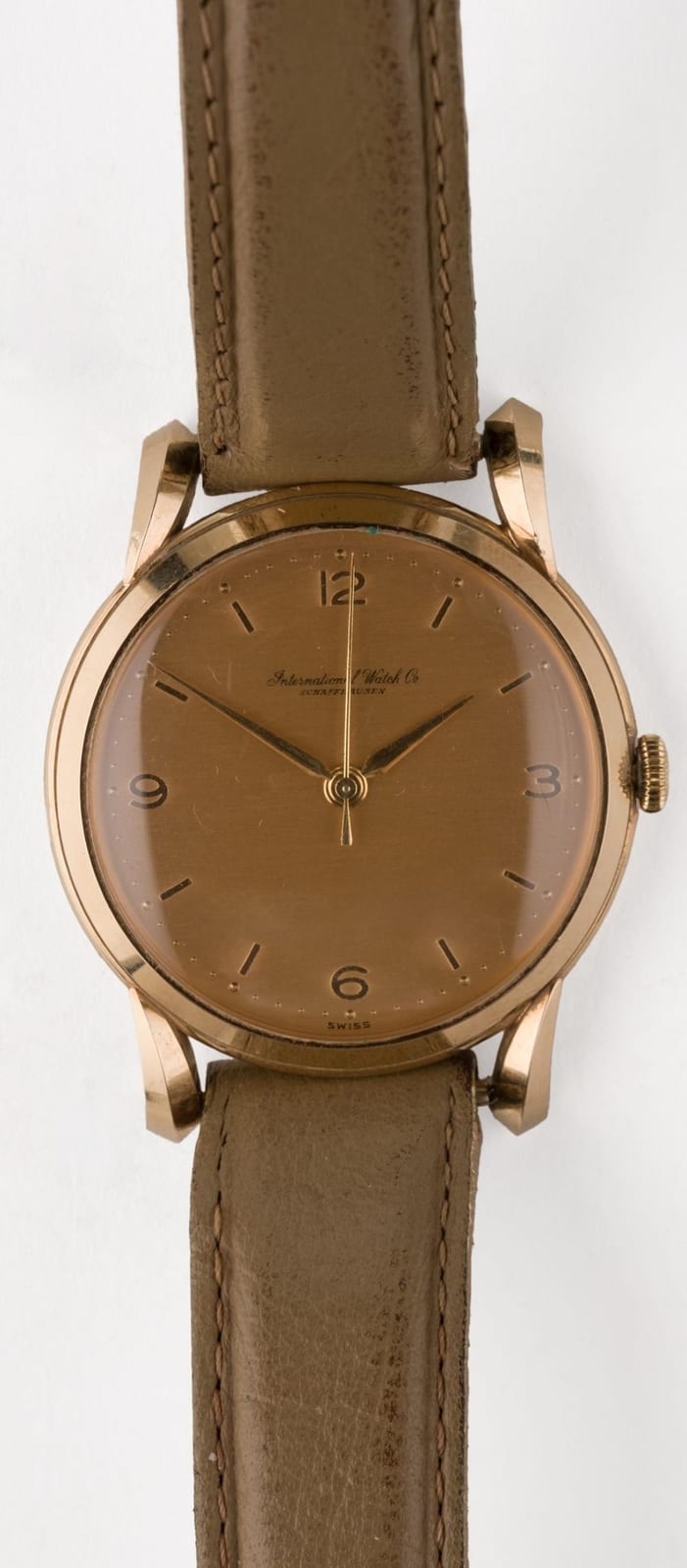 Gold wristwatch with a round dial and Arabic numeral markers, set on a brown leather strap.