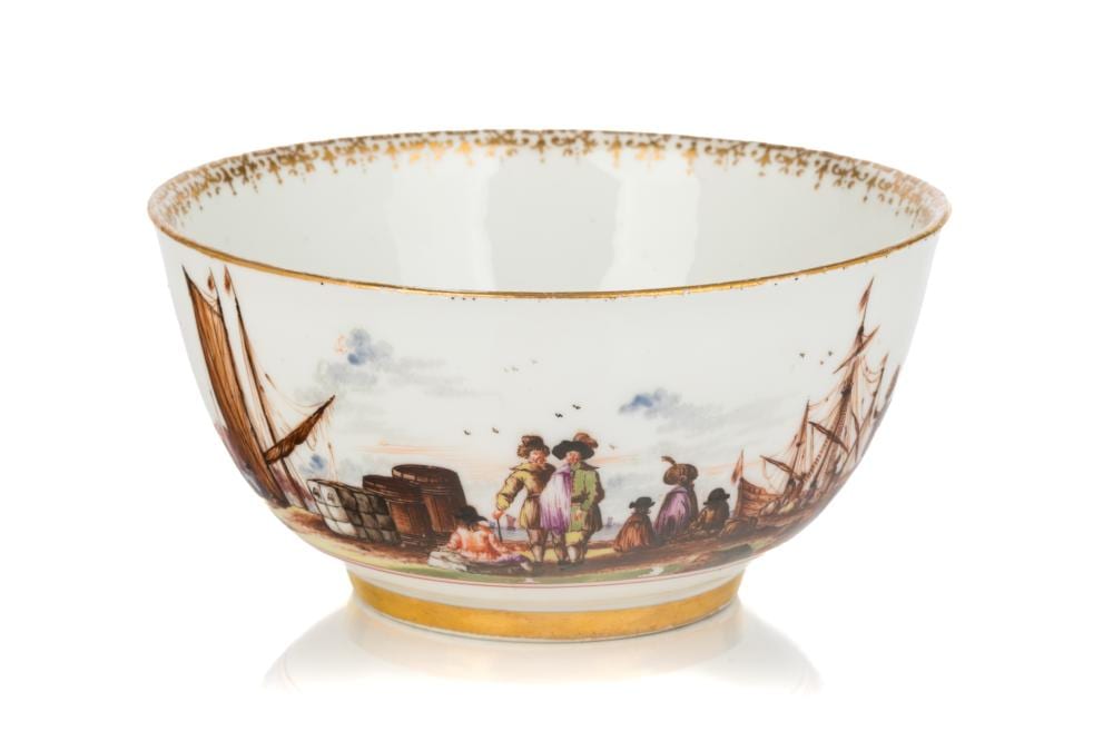 White porcelain bowl with a gold rim and painted figures near a dock, sailboats, and landscape scene on the outside.