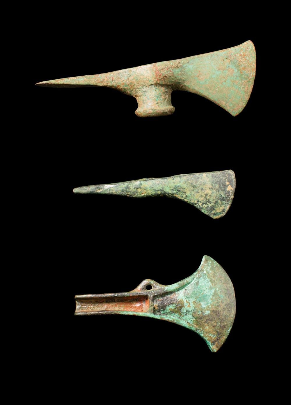 Three green patinated bronze axe heads on a black background, shown side and front views.