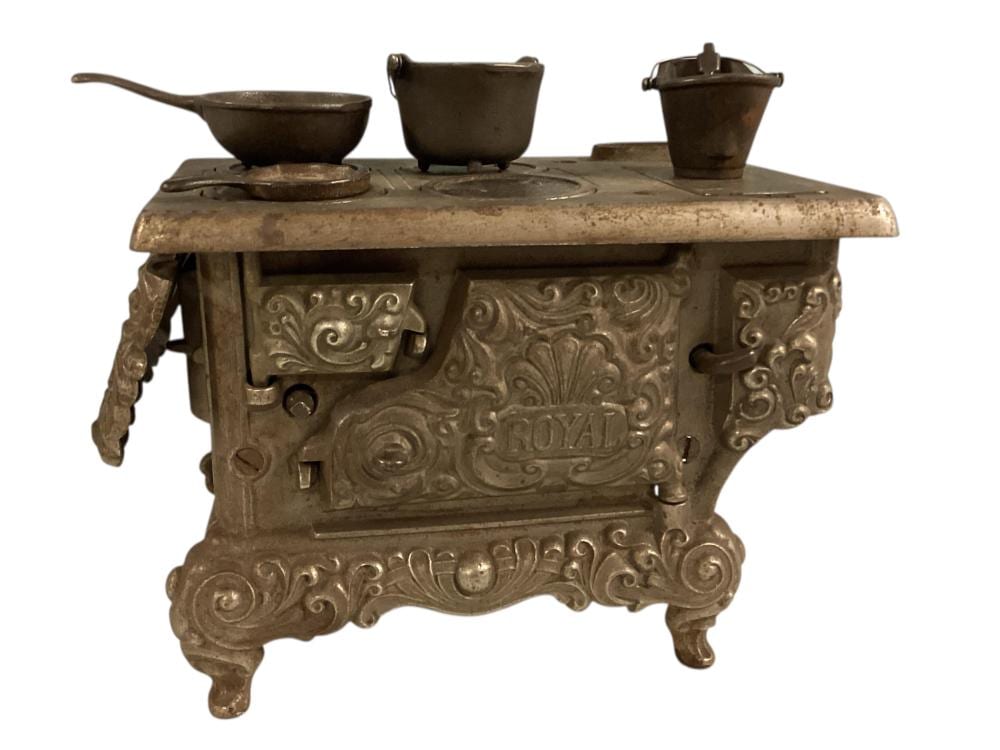 Cast iron toy stove with ornate embossed front panel and three small metal pots on top.