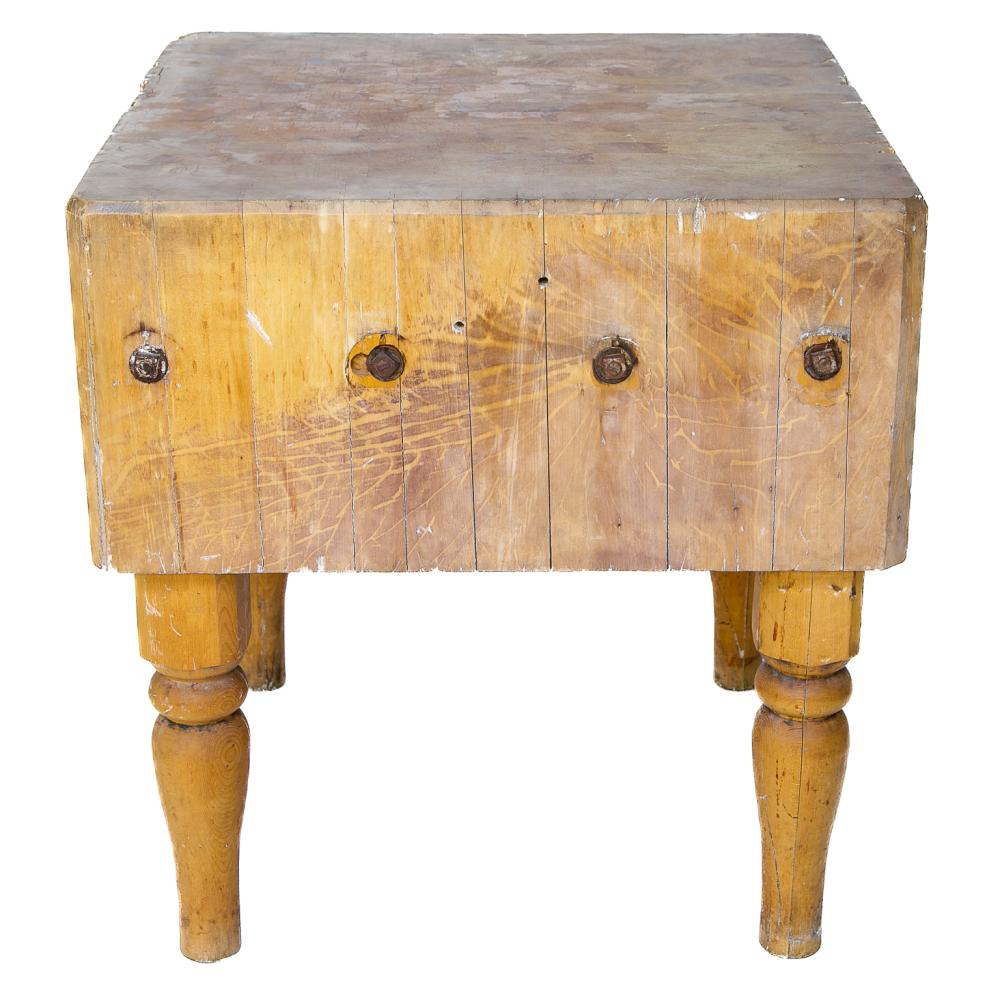 Wooden butcher block with a rectangular top and four turned legs, shown from the front, with metal hardware on the front panels.