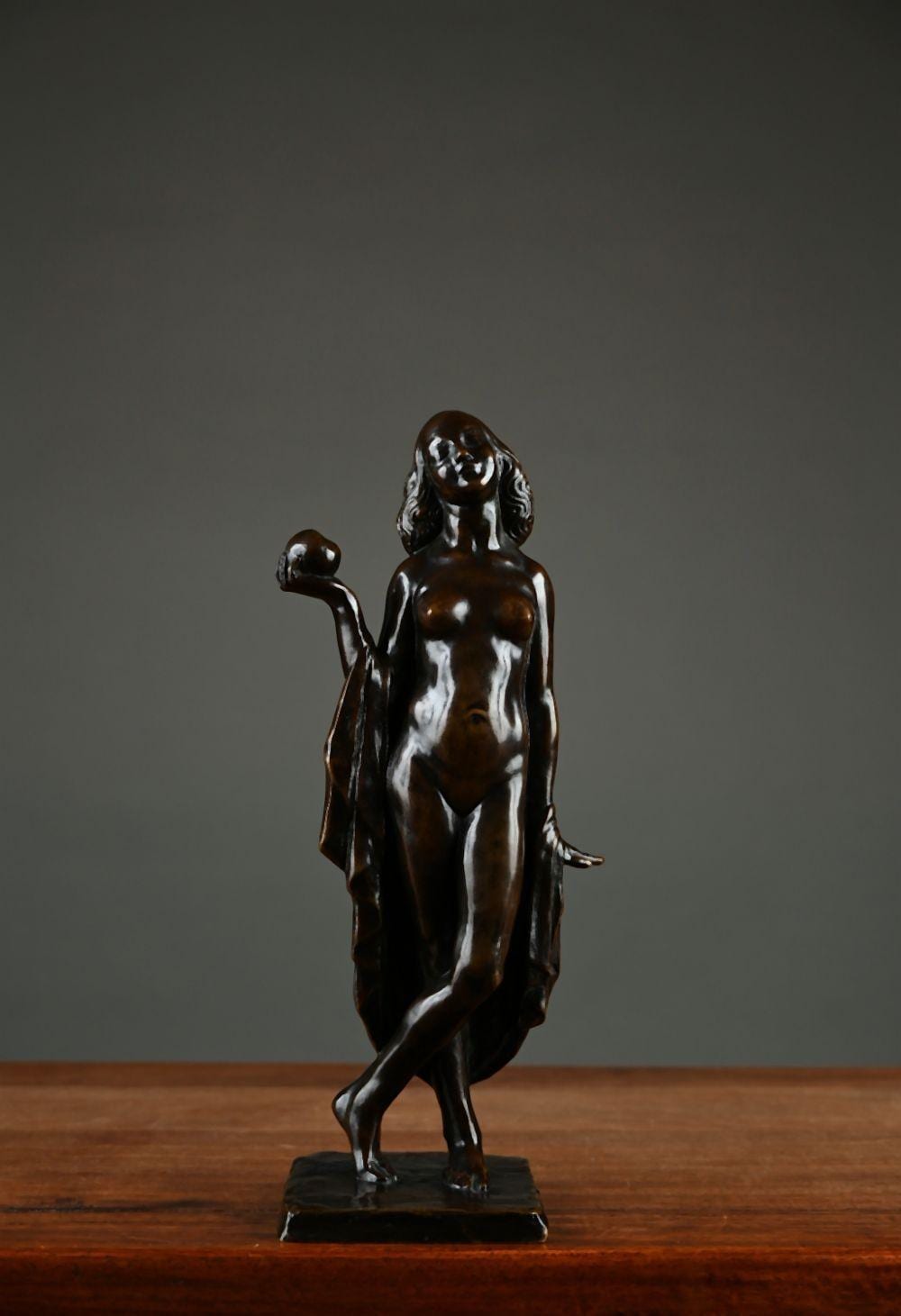 Bronze-style sculpture of a female nude standing with one arm raised and the other bent, displayed on a dark base.