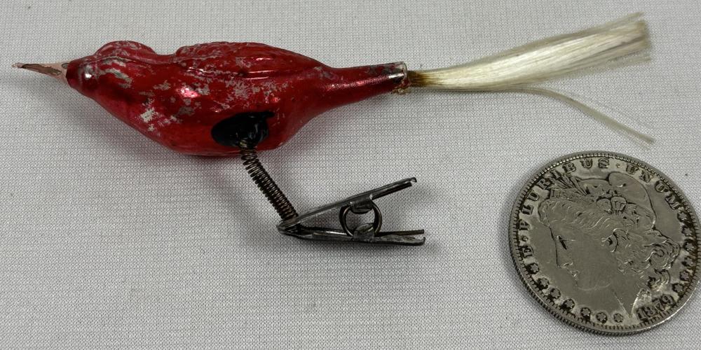 Red bird-shaped clip-on Christmas ornament with glittered surface and metal spring clip, shown next to a coin for size.