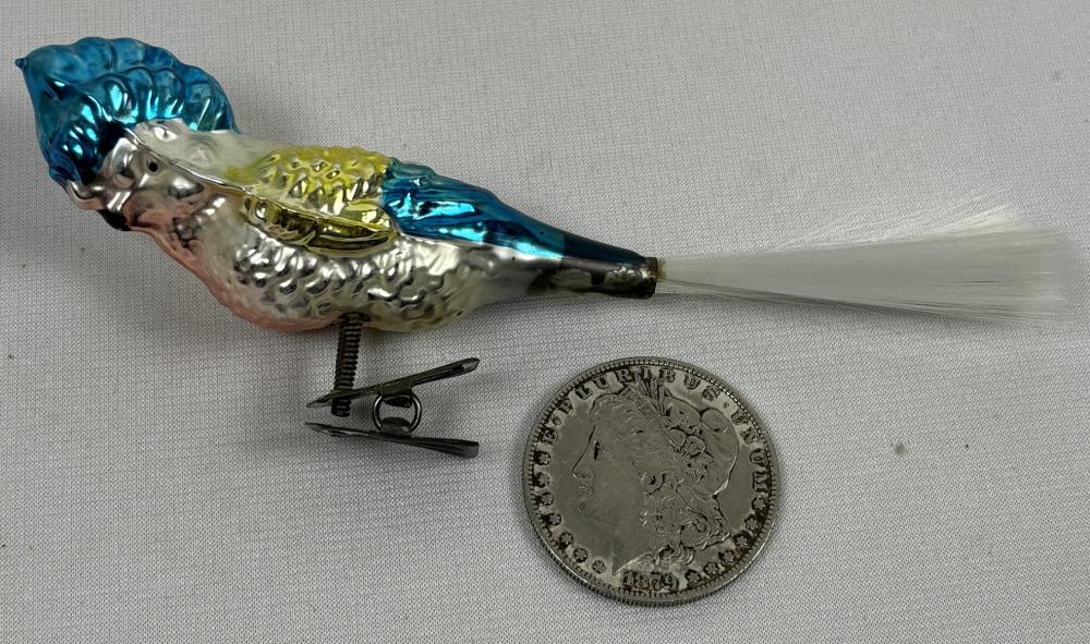 Blue and gold bird-shaped Christmas ornament with a clip base, photographed beside a U.S. coin for scale.