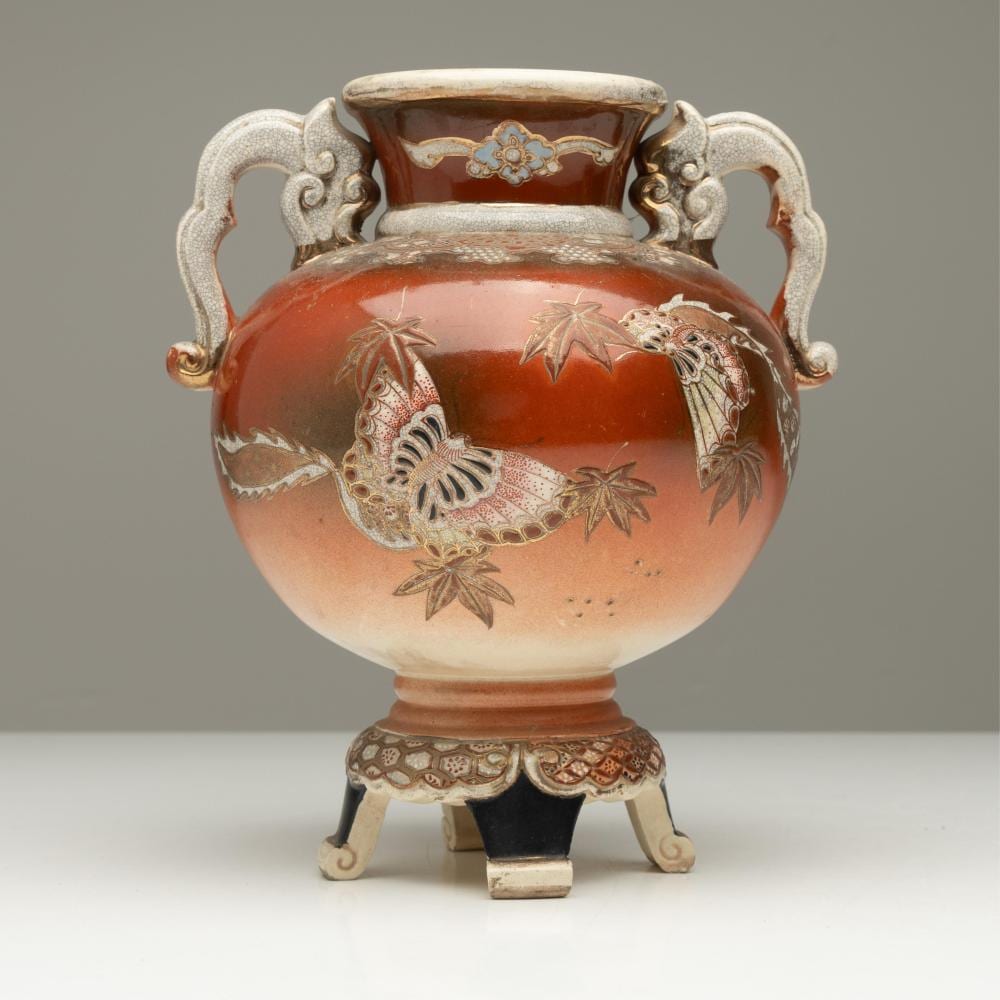 Front view of a twin-handled ceramic vase with an orange glaze and white floral-and-bird decoration on a light background.