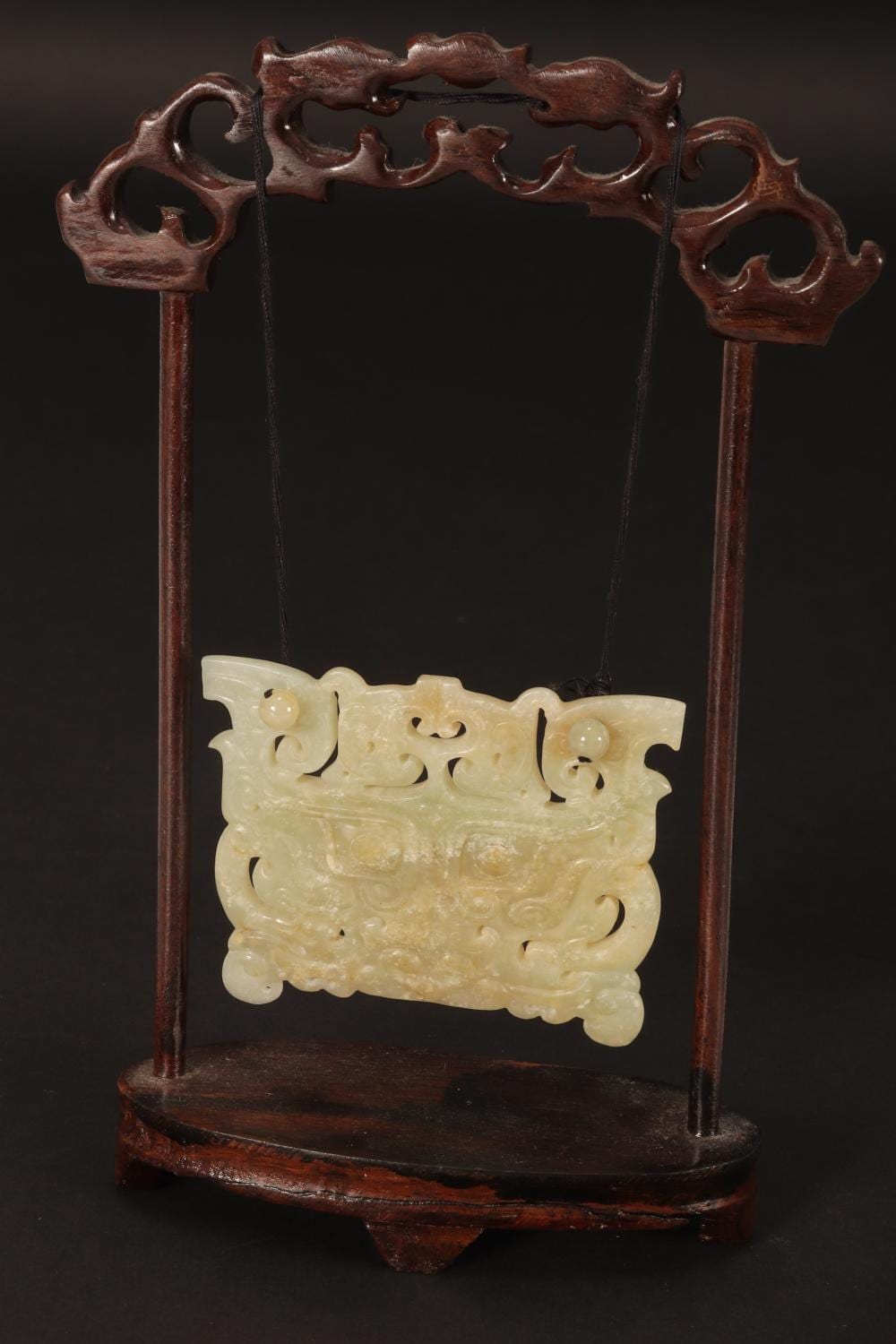 Carved pale jade-like plaque with intricate dragon-like motifs mounted on a dark wooden stand with two vertical posts.