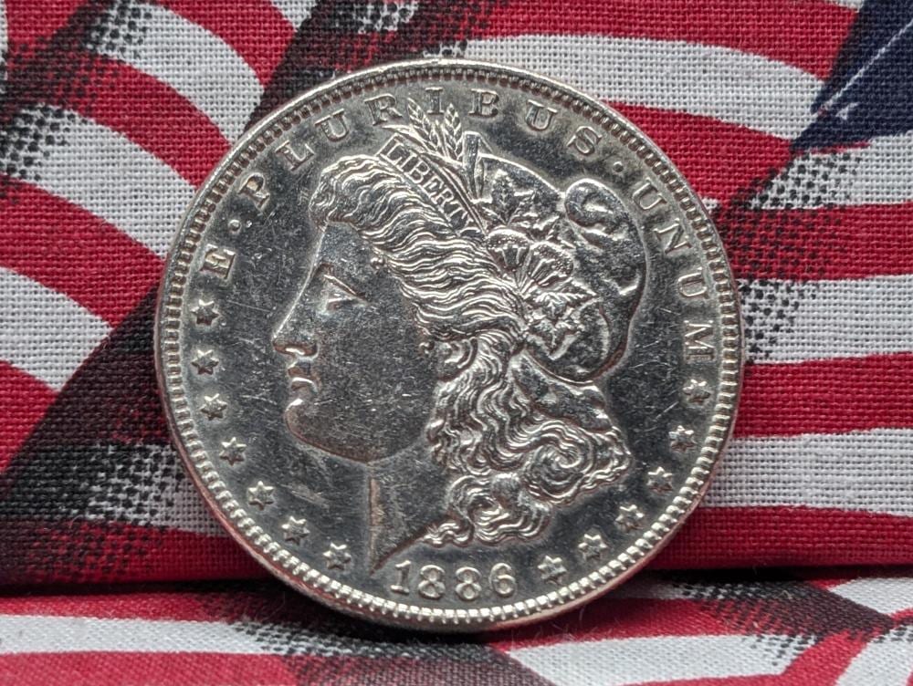 Close-up of a silver-colored Morgan dollar coin with a left-facing profile of Lady Liberty and the year 1886.
