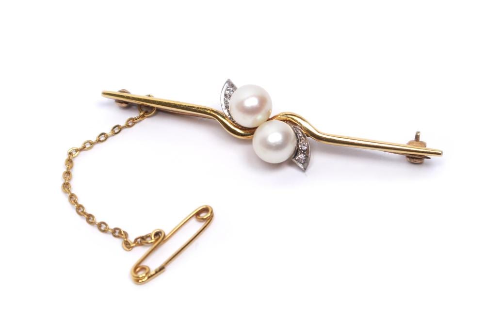 Gold-tone bar brooch with two white pearl-like beads and a small pavé diamond-like cluster on the center.