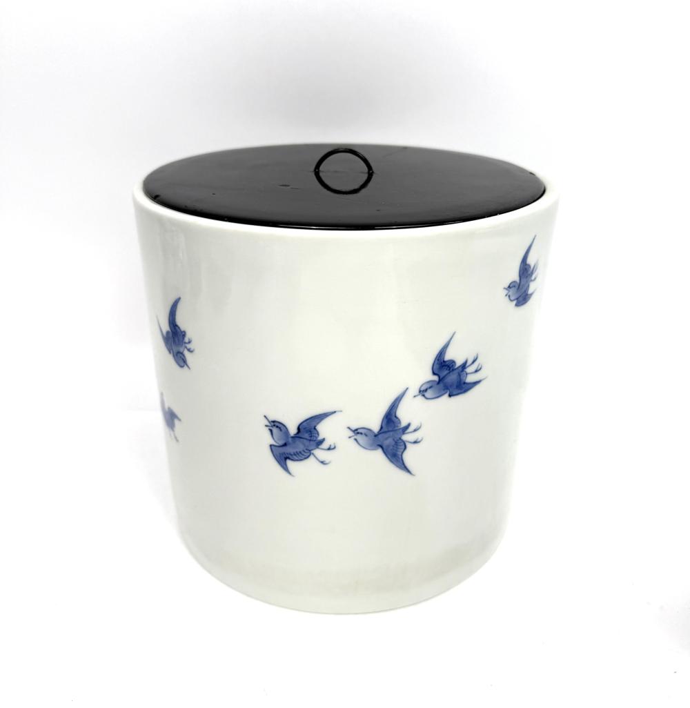 White porcelain lidded canister or water container with blue bird and branch decoration and a dark circular lid on top.