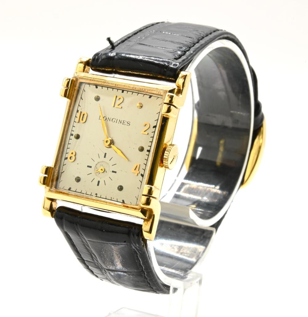 Gold rectangular wristwatch with a cream dial, black leather strap, and visible hands and numerals on a white display stand.