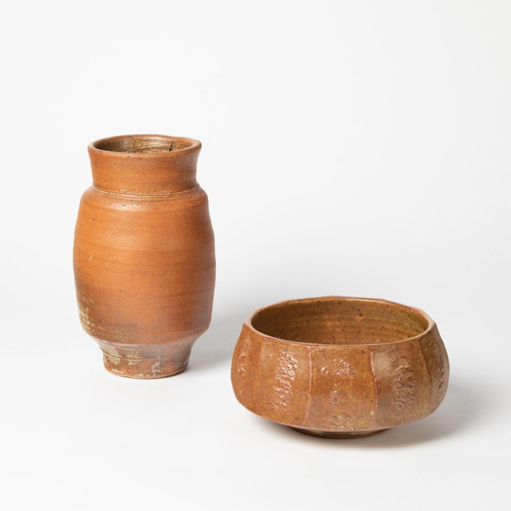 Two terracotta ceramic vessels on a white background: a rounded vase and a shallow bowl with speckled surface and raised foot.