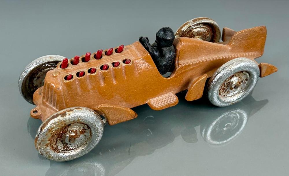 Cast iron toy rocket racer car with brown body, silver wheels, and a red row of studs along the top, with a black driver figure.