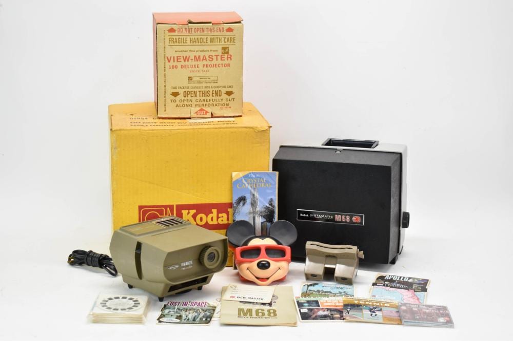 Vintage Kodak View-Master 100 deluxe movie projector with box, film reels, booklets, and accessories on a white background.