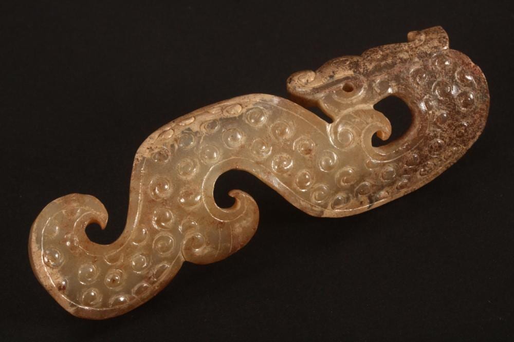 Close-up of a carved jade-like decorative object with curled spiral motifs and rounded pebble-like patterns on a dark background.