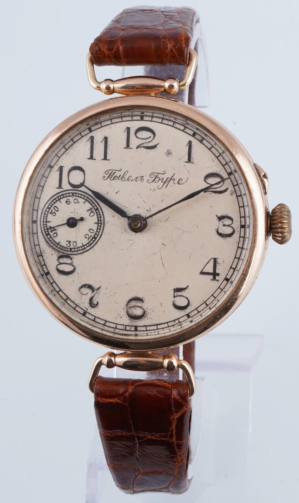 Close-up of a gold wristwatch with a white dial, black Arabic numerals, and black hour and minute hands.