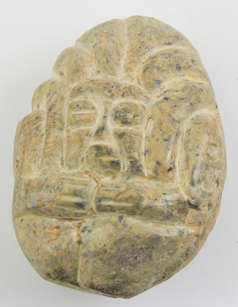 Close-up of a carved stone figure with a hooded, hunched form and incised facial features and clothing-like details.