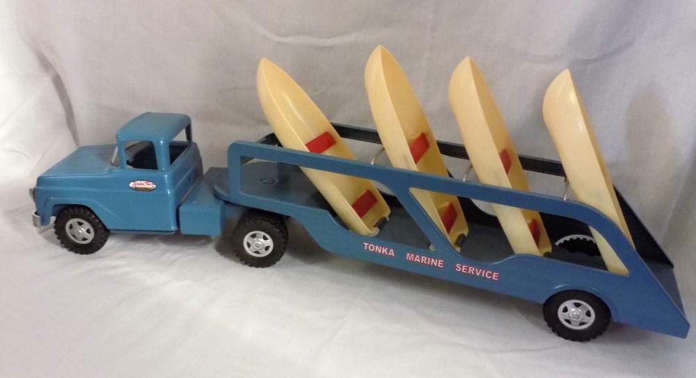 Blue toy truck with a long trailer carrying multiple pale yellow boats, labeled “TONKA” and “MARINE SERVICE.”