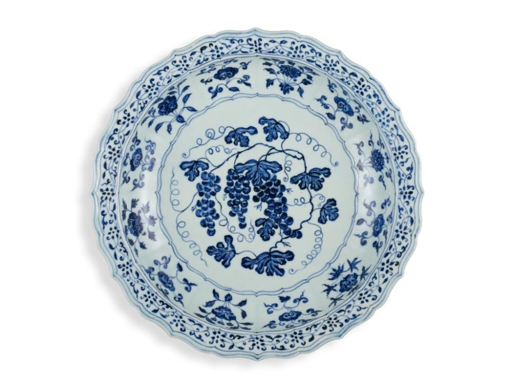 An exceptional and rare blue and white barbed 'grape' charger, Ming dynasty, Yongle period | 明永樂　青花葡萄紋折沿菱口盤 comparable sale
