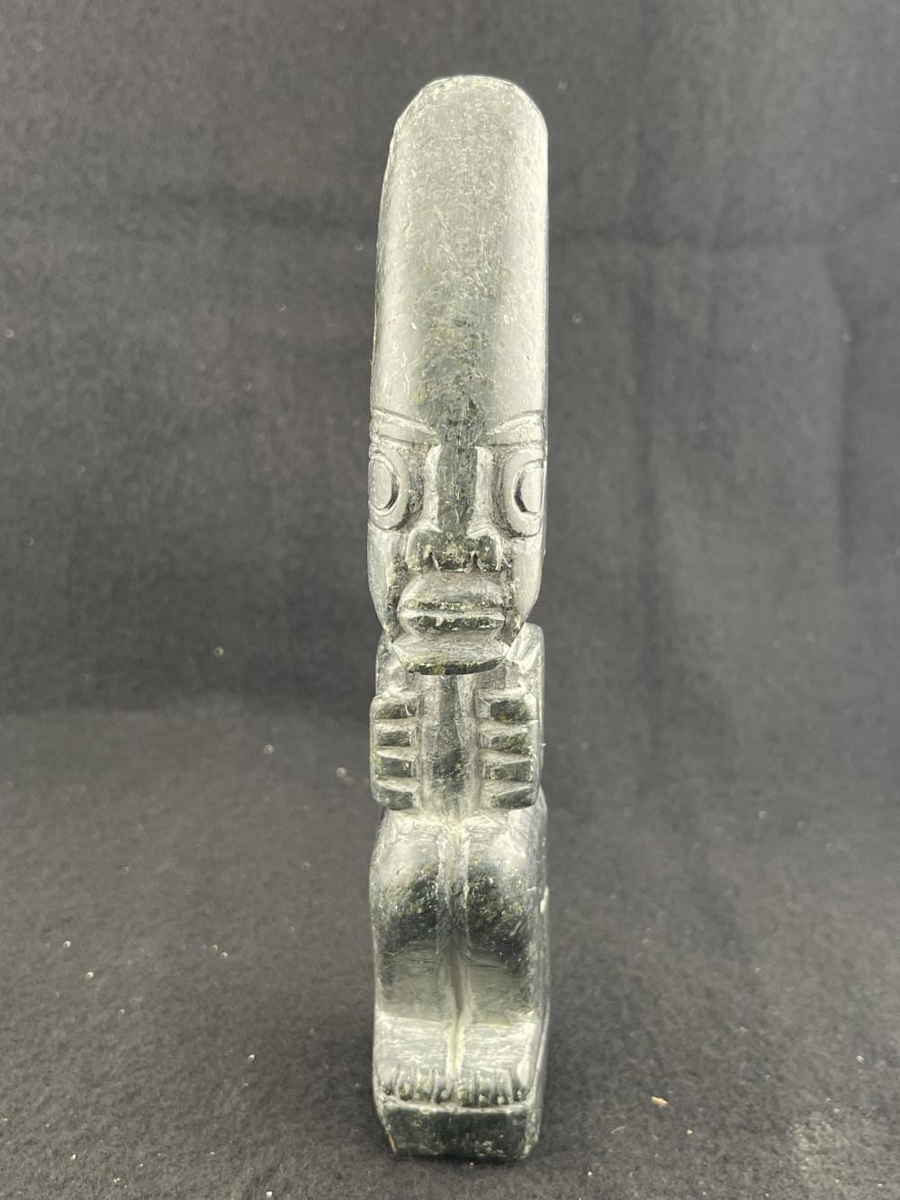 Carved stone figurine with a tall headdress and a stylized face, shown against a dark background.