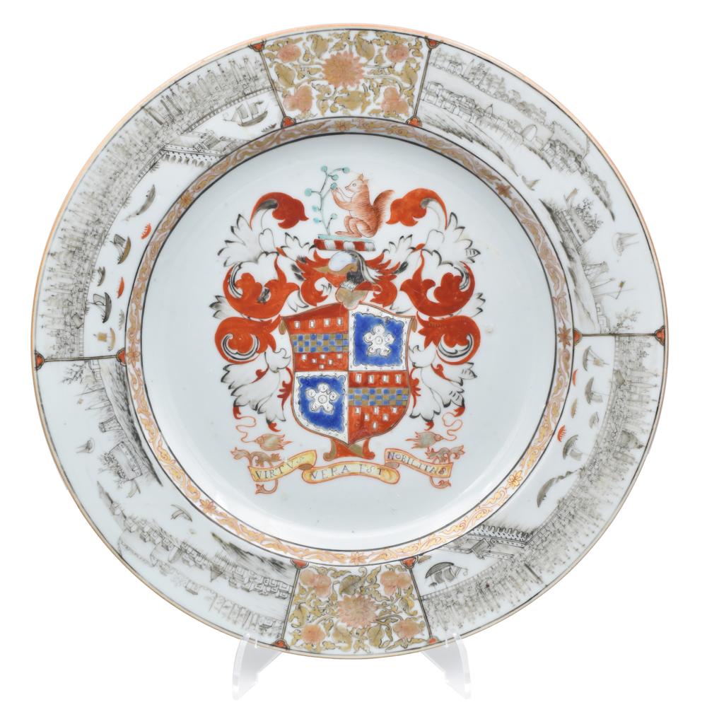 White porcelain plate with a central armorial crest in red, blue, and gold, surrounded by a detailed border of cityscape-style engravings and scrolling motifs.