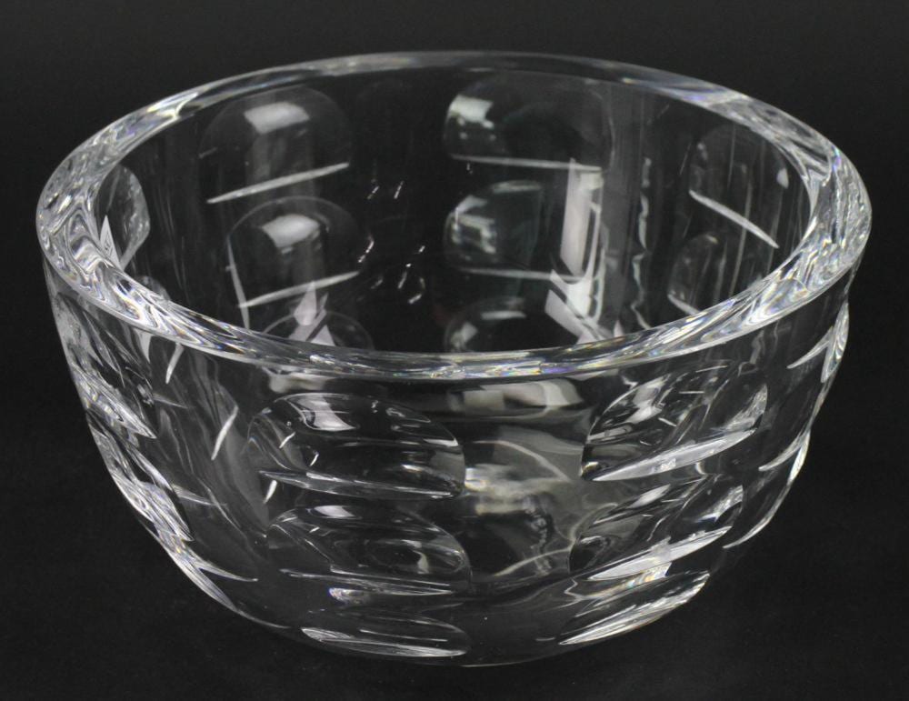 Clear crystal bowl with cut decorative pattern and faceted sides, photographed against a dark background.