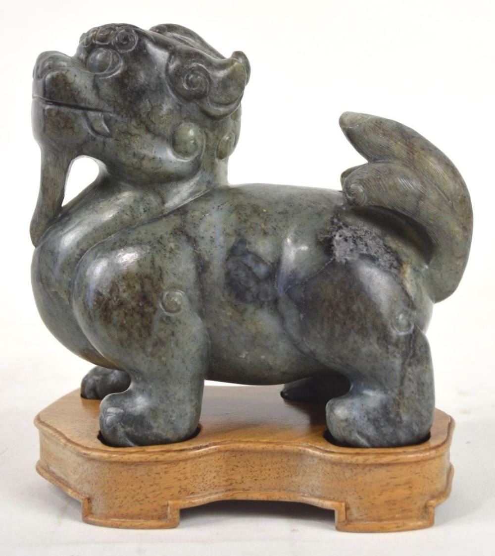 Carved stone foo dog sculpture standing on a small rectangular base with a curled tail and detailed face.
