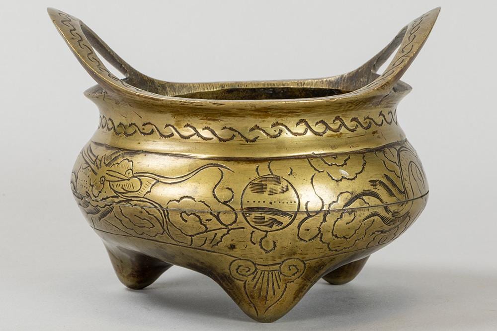 Gold-colored metal incense burner with three small legs, open bowl form, and engraved dragon and cloud motifs.