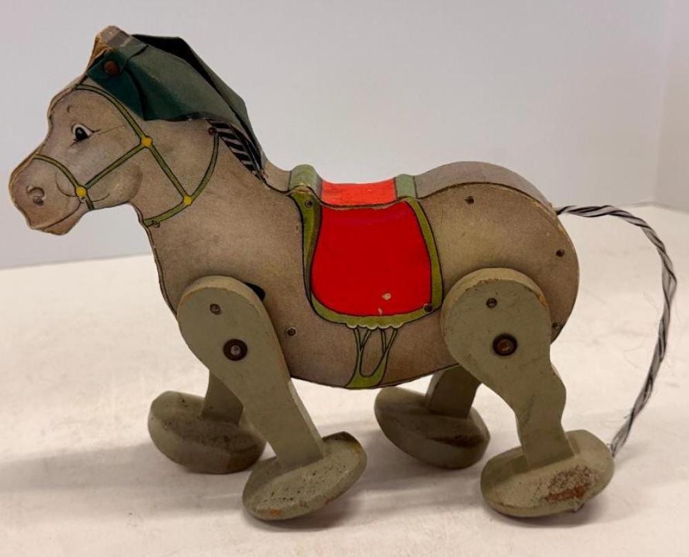 Vintage wind-up toy horse with a painted body, red saddle, and wooden wheels, standing on four legs with a string tail.